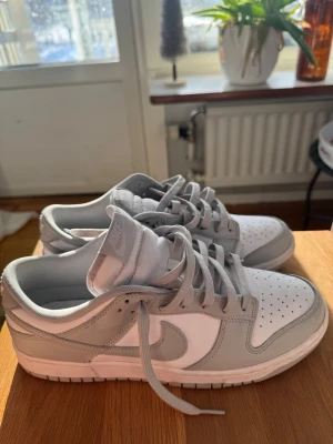 Nike Dunk Low grå/vita sneakers - Nike Dunk Low sneakers i mycket bra skick med extra creaseskydd. Är storlek 44 men är väldigt små i storleken, känns mer som 42/42,5