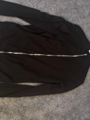 Svart ziptröja med hög krage - En stilren svart ziptröja med lång ärm och hög krage. Tröjan har dragkedja framtill och är tillverkad i ett mjukt, tunt material som passar perfekt till lager-på-lager. Enkel och clean design utan synliga loggor.