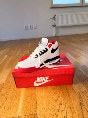 Nike Air Max vit/röd/svart sneaker - Nike Air Max sneaker med vit ovandel, röda detaljer och svart swoosh. Skon har en synlig Air Max-dämpning i sulan, klassiska snörningar och en robust design. Perfekt för dig som gillar sportig stil och ikoniska sneakers.