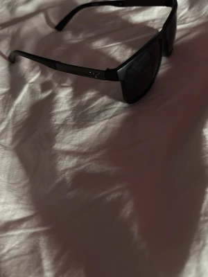 Svarta Armani solglasögon  - Snygga svarta solglasögon med breda bågar och rektangulär form. De har en sportig vibe och passar perfekt för dig som gillar en clean och stilren look. Lätta att matcha med olika outfits och ger ett coolt intryck.