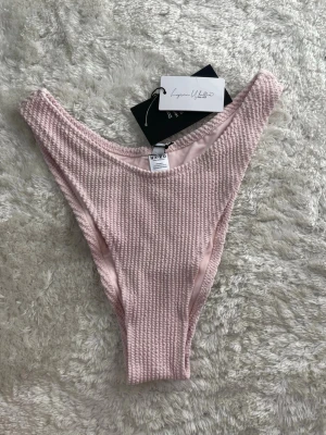 Ljusrosa ribbade bikiniunderdel NA-KD - Supersnygg ljusrosa bikiniunderdel från NA-KD med ribbad struktur. Modellen har hög midja och v-formad skärning framtill för en trendig look. Perfekt för dig som vill ha en enkel men ändå stilren bikiniunderdel till sommaren.