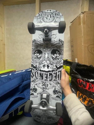 Skateboard med svartvit grafik - Cool skateboard från  hang ten med svartvit, detaljerad grafik och text. Brädan har svarta hjul och silverfärgade trucks. Perfekt för dig som gillar streetstyle och vill sticka ut med en unik design. 