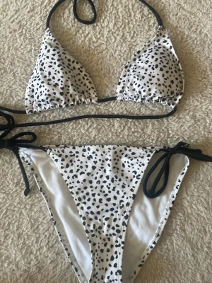 Vit bikini med svarta prickar - En fin bikini med svarta prickar och svart band, perfekt för stranden, poolen. Överdelen är i storlek M och underdelen i storlek S.