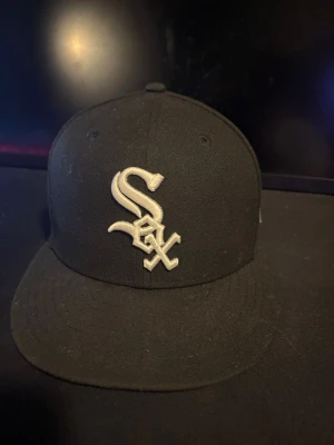 Svart White Sox keps från New Era - Säljer en svart 59FIFTY keps från New Era med Chicago White Sox-logga broderad i vitt framtill. Klassisk flat brim och officiell MLB On-Field modell. Perfekt för dig som gillar sportig streetwear och vill ha en stilren look.