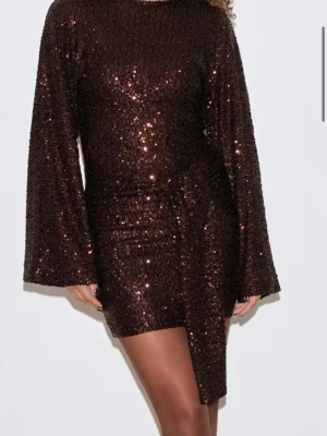 Brun glittrig kort klänning med knyt - Säljer en brun glittrig kort klänning med långa ärmar med knytning i midjan. Endast använd en gång på nyår. Nypris 699kr 