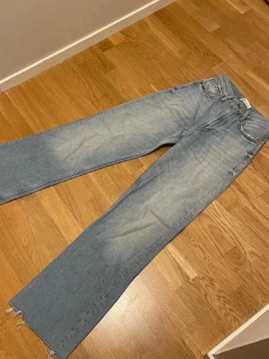 Ljusblå raka jeans från Zara - Säljer ett par ljusblå jeans från Zara med rak passform och råa, fransiga benslut. Jeansen har klassisk femficksdesign och är tillverkade i denim. Perfekta för dig som gillar en avslappnad och trendig look.