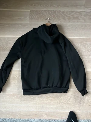 Svart hoodie med spindelnätsmotiv - Säljer en svart hoodie med stor spindelnätsgrafik på framsidan, dekorerad med färgglada detaljer och text i rosa. Hoodien har huva och känguruficka framtill. Materialet ser ut att vara mjukt och stretchigt, perfekt för en avslappnad streetwear-look. Stor stl.