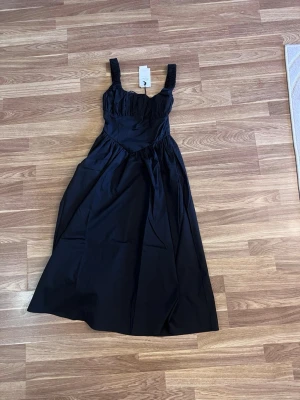 corset dress - En elegant svart långklänning från Gina Tricot med breda, rynkade axelband och markerad midja. Klänningen har ett stilrent och klassiskt snitt med lätt rynkade detaljer upptill och ett flödande fall. Perfekt för dig som vill ha en tidlös look. Slutsåld!