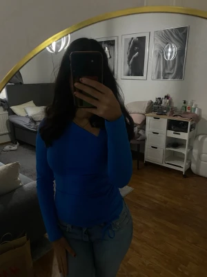 Blå långärmad v-ringad topp - Snygg blå långärmad topp med v-ringning och slim passform. Perfekt att matcha med jeans för en cool och enkel look. Toppens material känns mjukt och stretchigt, vilket gör den bekväm att bära hela dagen.