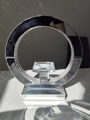 Modern cirkelformad glaskristall prydnad - Säljer en unik cirkelformad prydnad i transparent glaskristall med geometriska detaljer och en fyrkantig kristall i mitten. Står på en stabil rektangulär fot och reflekterar ljus snyggt. Perfekt som dekorativt inslag i hemmet.