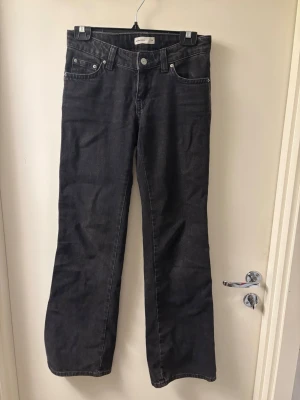 Svarta bootcut jeans från Gina tricot - Säljer ett par svarta bootcut jeans från gina tricot med klassiska femficksdetaljer och knappar på bakfickorna. Jeansen har normal passform och är tillverkade i bomull. Perfekta för dig som gillar en tidlös och cool look.