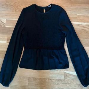 Långärmad blus med smock! - Långärmad blus med långa ärmar. Smock som avslutas med en volangkant. Lite vidare ärmar och resår i ärmslut. I 100% viskos. Axelbredd 36 cm, längd 56 cm. Använd några gånger. Inga skavanker!  