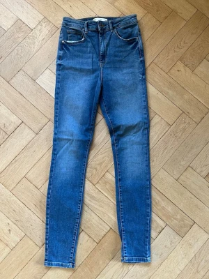 Blå skinny jeans med hög midja - Säljer ett par blå skinny jeans med hög midja och klassiska fem fickor. Från Gina Tricot i modellen Gina, strl 38.
