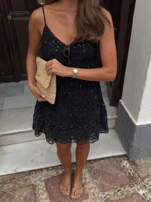 Svart spetsklänning med smala band - Supersöt svart kortklänning med tunna axelband och v-ringning. Klänningen har ett detaljerat spetsmönster, paljetter och pärlor. 
