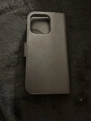 Svart plånboksfodral till mobil - Säljer ett svart plånboksfodral till mobil med magnetlås och plats för kort. Fodralet är tillverkat i konstläder och har en stilren design med rundade hörn och öppning för kameran. Perfekt för dig som vill ha både skydd och funktion.