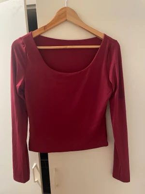 Vinröd långärmad topp med bred urringning - En enkel och stilren vinröd topp med bred urringning och långa ärmar. Modellen är croppad och har en slim passform som framhäver siluetten. Perfekt att matcha med jeans eller kjol för en trendig look.