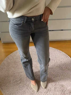 Grå raka jeans med klassisk passform - Säljer ett par grå jeans med raka ben och klassisk femficksdesign. Jeansen har normal midja och silverfärgad knapp framtill. Materialet är denim och färgen är en snygg grå nyans som är lätt att matcha. Perfekt för dig som gillar en enkel och stilren look.