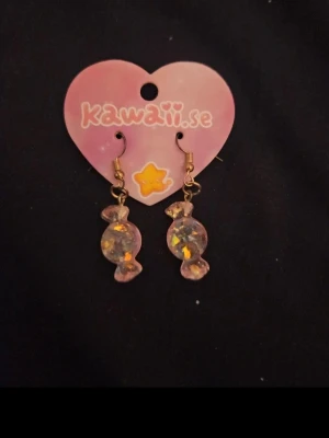 Glittriga godisörhängen från Kawaii.se - Säljer ett par supersöta örhängen från Kawaii.se formade som godisbitar. De är transparenta med glittriga inslag i olika färger och har en lekfull design som verkligen sticker ut. Perfekta för dig som gillar kawaii-stilen och vill ha något unikt.