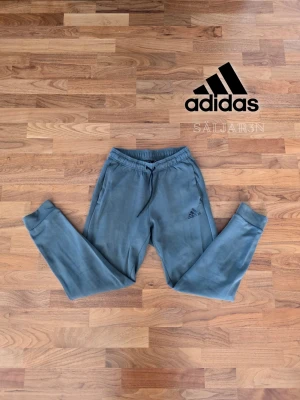 Grå mjukisbyxor från Adidas - 👖 Adidas Sweatpants – Storlek S 👖 Bekväma och stilrena Adidas-byxor i blå nyans. Elastisk midja med dragsko ger perfekt passform och muddarna vid bensluten håller byxorna på plats. Perfekta för träning, vardag eller lounge-stil. Byxorna är i nyskick och kombinerar sportig design med komfort. Praktiska och lättmatchade – ett måste för både aktivt och avslappnat användande. 📦 Snabb leverans – Kontakta för frågor!