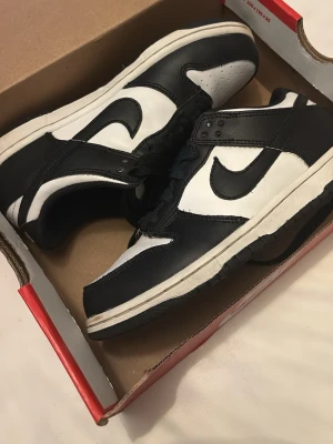 Nike Dunk Low pandas 34 - Nike Dunk Low sneakers i svart och vitt läder med klassisk Swoosh-logga på sidan. Lågt skaft och vit sula med svarta detaljer. Perfekt för dig som gillar stilrena och tidlösa sneakers med streetwear-vibe.