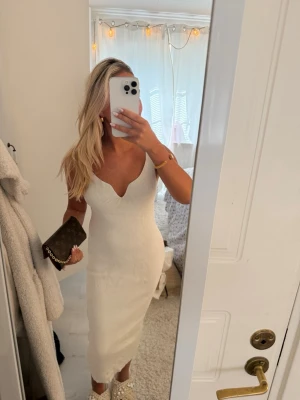 Vit ribbad långklänning - Säljer en snygg vit ribbad långklänning med v-ringad urringning och ärmlös design. Klänningen har en kroppsnära passform och är perfekt för sommarens alla tillfällen. Materialet är stretchigt och bekvämt, vilket ger en smickrande siluett.