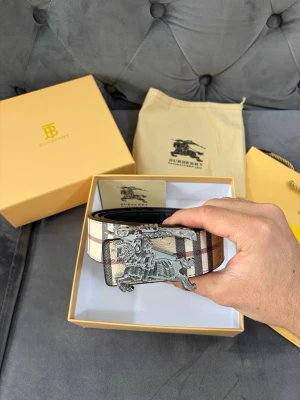 Burberry bälte - Säljer ett exklusivt bälte från Burberry med klassiskt rutigt mönster i beige, brun, svart och vit. Bältet har en unik silverfärgad spänne med Burberrys ikoniska ryttare. Perfekt för att lyfta din outfit med en lyxig touch.
