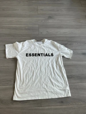 Vit Essentials t-shirt med tryck - Vit t-shirt från Essentials med svart texttryck över bröstet. Klassisk rund halsringning och korta ärmar. Tillverkad i mjuk bomull för en skön och avslappnad stil.