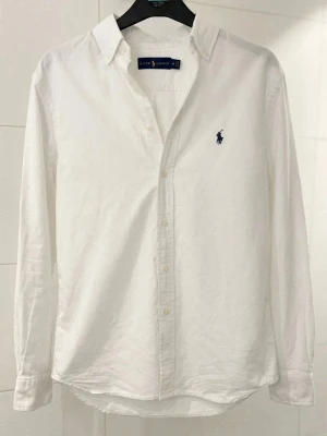Vit Ralph Lauren skjorta - Vit Ralph Lauren skjorta i storlek M. Skjortan har använts 3 gånger och är i jättefint skick. Det är en riktigt schysst skjorta perfekt till sommaren. Det är bara att höra av sig vid frågor eller funderingar🙌