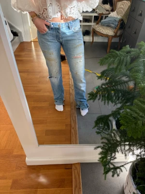 Ljusblå raka jeans med slitningar - Säljer ett par ljusblå jeans med raka ben och slitna detaljer på både fram- och baksida. Jeansen har klassisk femficksmodell och låg midja. Perfekta för en avslappnad och trendig look.