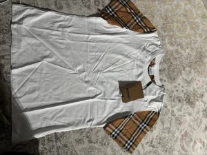 Vit Burberry t-shirt - Snygg vit t-shirt från Burberry med klassiska beige, svarta och röda rutiga ärmar. T-shirten har rund halsringning och är tillverkad i mjuk bomull. Perfekt för dig som gillar stilrena plagg med en twist.