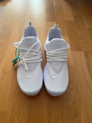 Vita Nike air Preston  - Fräscha helvita Nike Presto sneakers med minimalistisk design och diskret Nike-logga på tån. Ovandel i mesh för bra andningsförmåga och bekväm passform. Klassiska vita skosnören och flexibel sula gör dem perfekta för en clean streetstyle-look. Storlek 46 men passar 45