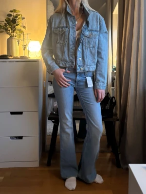 Ljusblå jeansjacka från Mango! - Säljer en ljusblå jeansjacka i klassisk modell med raka axlar och två bröstfickor med lock och knapp. Jackan har silverfärgade knappar framtill och vid ärmsluten. Snygg, tidlös och enkel att styla till olika looks. Perfekt för dig som gillar en avslappnad men trendig vibe.