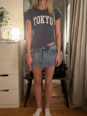 Blå jeanskjol med fransig kant - Säljer en kort blå jeanskjol med rå, fransig kant och klassiska fickor fram och bak. Kjolen har en avslappnad passform och är gjord i denim. Perfekt för dig som gillar en casual och trendig stil.