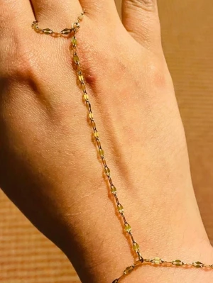 Guldigt handkedjearmband - Snyggt handkedjearmband i guldton som kopplar ihop en tunn kedja runt fingret och handleden. Kedjan har små dekorativa detaljer och ger en trendig och elegant look. Perfekt accessoar för att lyfta din outfit.