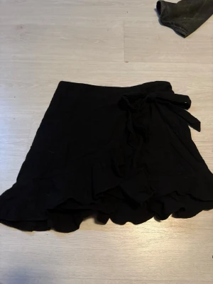 Svart omlottkjol med volang - Snygg svart kort omlottkjol med volangkant och knyt i midjan. Kjolen har en feminin och trendig look som passar perfekt till många olika stilar. Enkel att matcha med både toppar och tröjor.tveka inte att höra av er vid frågor eller funderingar😇💕