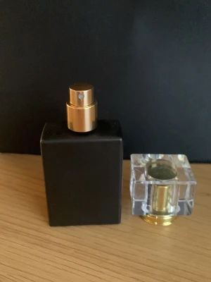 Elegant svart parfymflaska med guld - Snygg parfymflaska i matt svart med guldfärgad spraydel och en transparent fyrkantig kork med gulddetaljer. Flaskan har en stilren och modern design och levereras i en svart ask. 30 ml flaska som jag fyller på med en parfym ni vill ha och får 5 ml flaska på köpet.