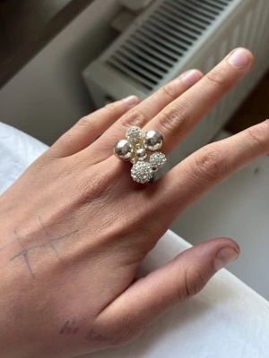 Statementring med pärlor och silverkulor - Unik statementring i silverfärg med stora blanka kulor och glittrande pärlor som bildar ett coolt kluster. Ringen har en modern och iögonfallande design som verkligen sticker ut. Perfekt för dig som gillar att bära något extra speciellt.