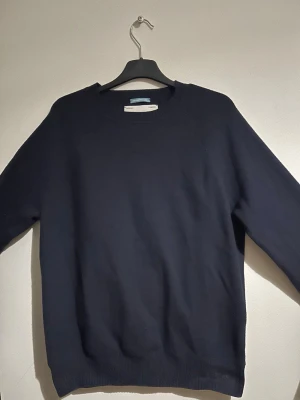 Mörkblå stickad tröja från Replay - Snygg mörkblå stickad tröja från Replay med rund halsringning. Tröjan har långa ärmar och ribbade muddar vid ärmslut och nederkant. Perfekt för dig som gillar stilrena och klassiska plagg.