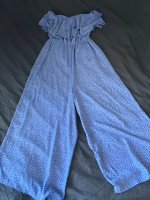 Ljusblå prickig jumpsuit Bik Bok - Supersöt ljusblå jumpsuit från Bik Bok med svarta prickar, off shoulder-modell och volang upptill. Vida ben och resår i midjan för en bekväm passform. Perfekt för dig som gillar en lekfull och trendig stil.