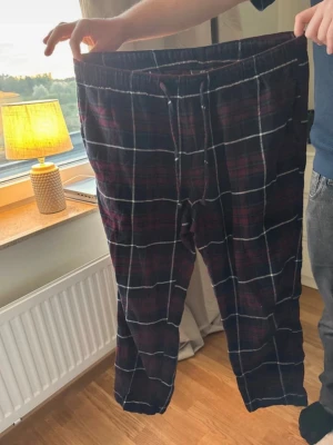 Rutiga pyjamasbyxor i mörka färger - Mysiga pyjamasbyxor med rutigt mönster i mörkblått, vinrött och vitt. Byxorna har resår i midjan och dragsko för bästa passform. Perfekta för chillkvällar hemma. Materialet känns mjukt och bekvämt mot huden.