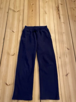 Mörkblå mjukisbyxor från Gina Tricot - Mörkblå mjukisbyxor från Gina Tricot med resår i midjan och dragsko. Byxorna har raka ben och är tillverkade i ett mjukt, bekvämt material som passar perfekt för chill dagar. Enkla att matcha med hoodies eller t-shirts.