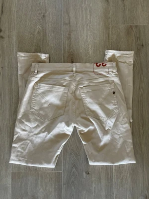 Dondup jeans - Snygga beige jeans från Dondup med klassisk femficksmodell och raka ben. Jeansen har diskreta nitar och en röd detalj på baksidan. Tillverkade i bomull med en stilren look som passar till det mesta.