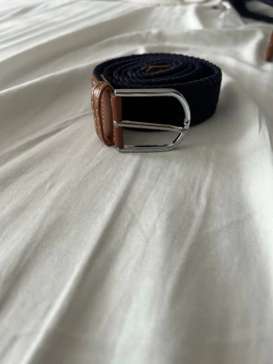 Mörkblå flätat bälte med skinn-detaljer - Helt nytt stretchigt flätat bälte, bältet är helt oanvänt och har plasten kvar, passar till nästan allt och passar alla storlekar då bältet är stretchigt