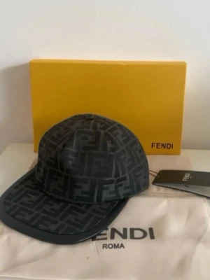 Svart keps - Snygg svart keps med det klassiska FF-monogrammet över hela kepsen. Kepsen har böjd skärm och justerbar baksida. Tillverkad i ett glansigt material som ger en lyxig känsla. Perfekt för dig som gillar exklusiva accessoarer.