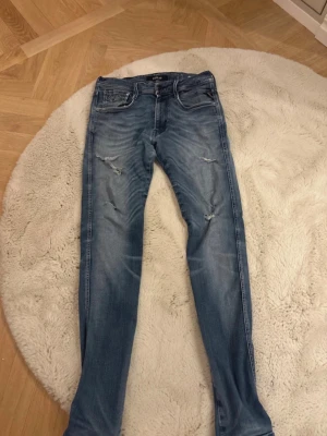 Replay ljusblå slitna jeans herr - Säljer ett par ljusblå jeans från Replay, modell Anbass. Jeansen har skinny fit, slitningar på låren och knäna samt klassisk femficksdesign. Perfekta för en avslappnad och trendig look. Materialet är denim i bomullsblandning.