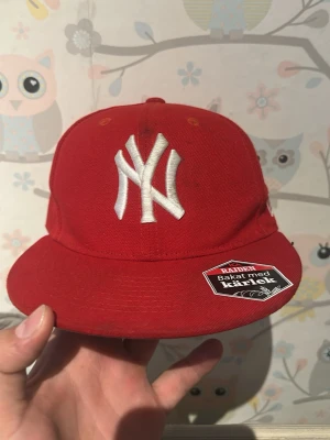 Röd New Era NY Yankees keps  - Säljer en röd New Era 59FIFTY keps med vit NY Yankees-logga framtill. Klassisk flat brim och broderade ventilationshål. Kepsen är gjord i bomull och har autentiska etiketter kvar på insidan.
