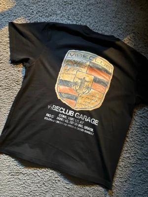 Svart t-shirt från Vibeclub Atelier - Helt ny. Svart t-shirt från Vibeclub Atelier med stor färgglad grafik och text på ryggen. T-shirten har klassisk passform och rund hals. Materialet är mjukt och skönt, perfekt för en avslappnad stil. Märket och trycket ger en unik vibe. Pris kan självklart diskuteras!