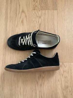 Margiela Gats -  Margiela GATs  Clean  sneaker som funkar till typ allt. Svart mocka med ljusa snören och klassisk gummisula. Enkel men fortfarande lyxig.  Skorna är i bra skick, bara normala användningsspår (kolla bilder). Bekväma och lätta att styla – funkar både vardag och lite mer dressat.  Säljer för att de inte används längre. Skriv om du vill ha fler bilder eller undrar nåt  prisk kan diskuteras!!!