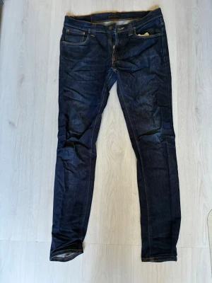 Mörkblå jeans från Nudie Jeans - Säljer ett par mörkblå jeans från Nudie. Jeansen har passformen lean dean och är i storleken W33 L34 men sitter mer som W32 L34. Vid minsta fundering hör av dig 🙌