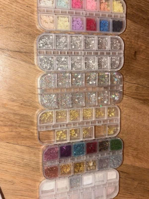 Nageldekorationer i mixade färger - Nageldekorationer i olika färger och former, inklusive glitter, stenar, paljetter och pärlor. Perfekt för att skapa unika och kreativa nageldesigner. Kommer i praktiska förvaringsaskar med många fack för enkel översikt. 15kr styck!💞